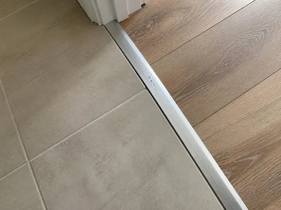 A thin metal transition strip marking the floor junction between two different tiles